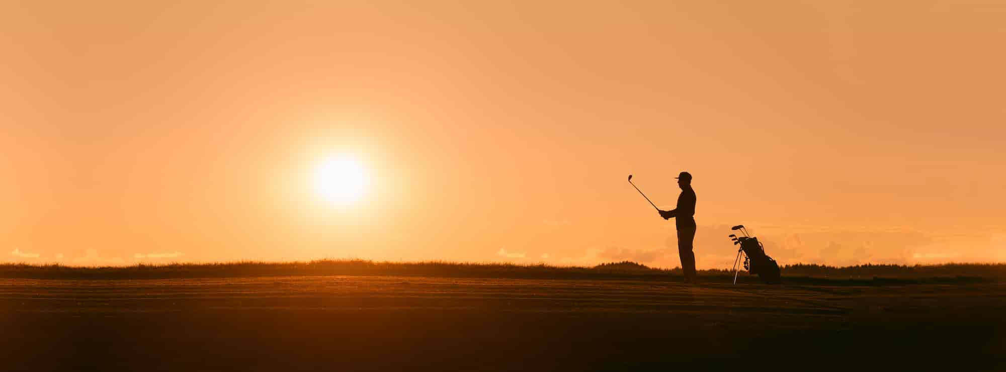 A golfer lines up a shot as the sun sets.